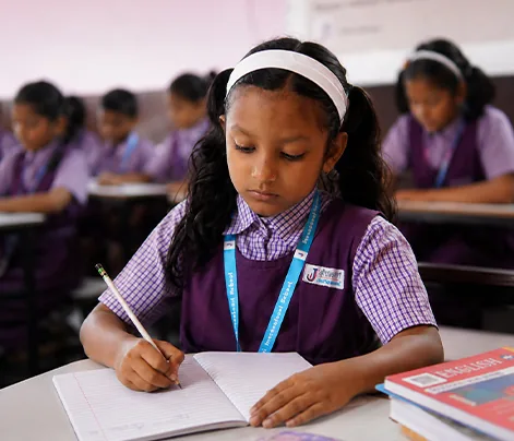 Girls in school uniform seated on the floor of a hall with their hands folded